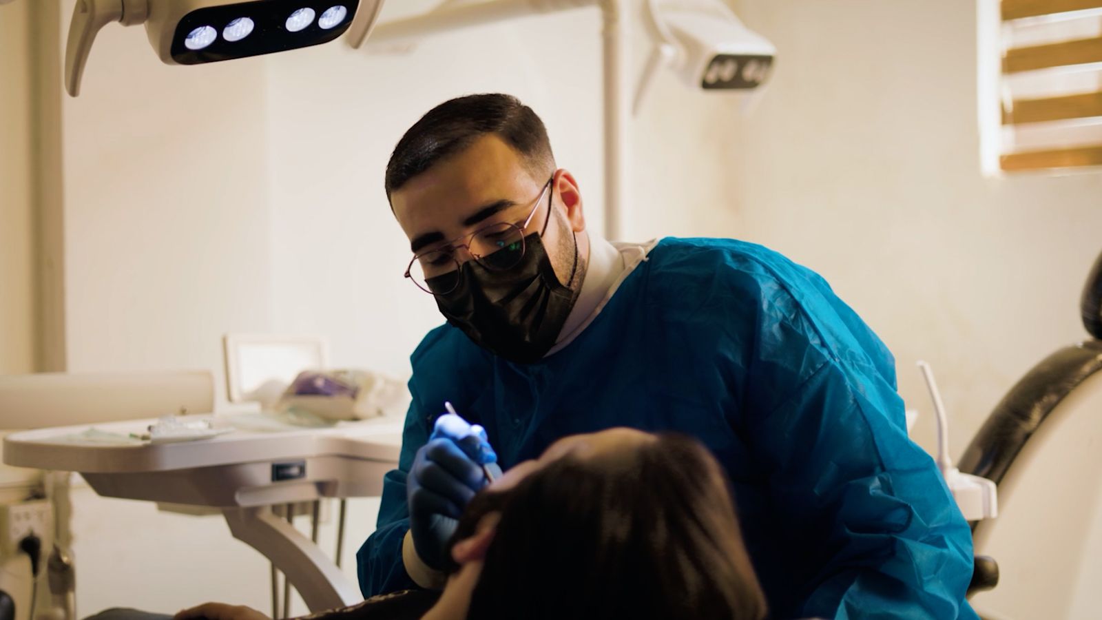 A dentist in a blue gown and mask treating a patient