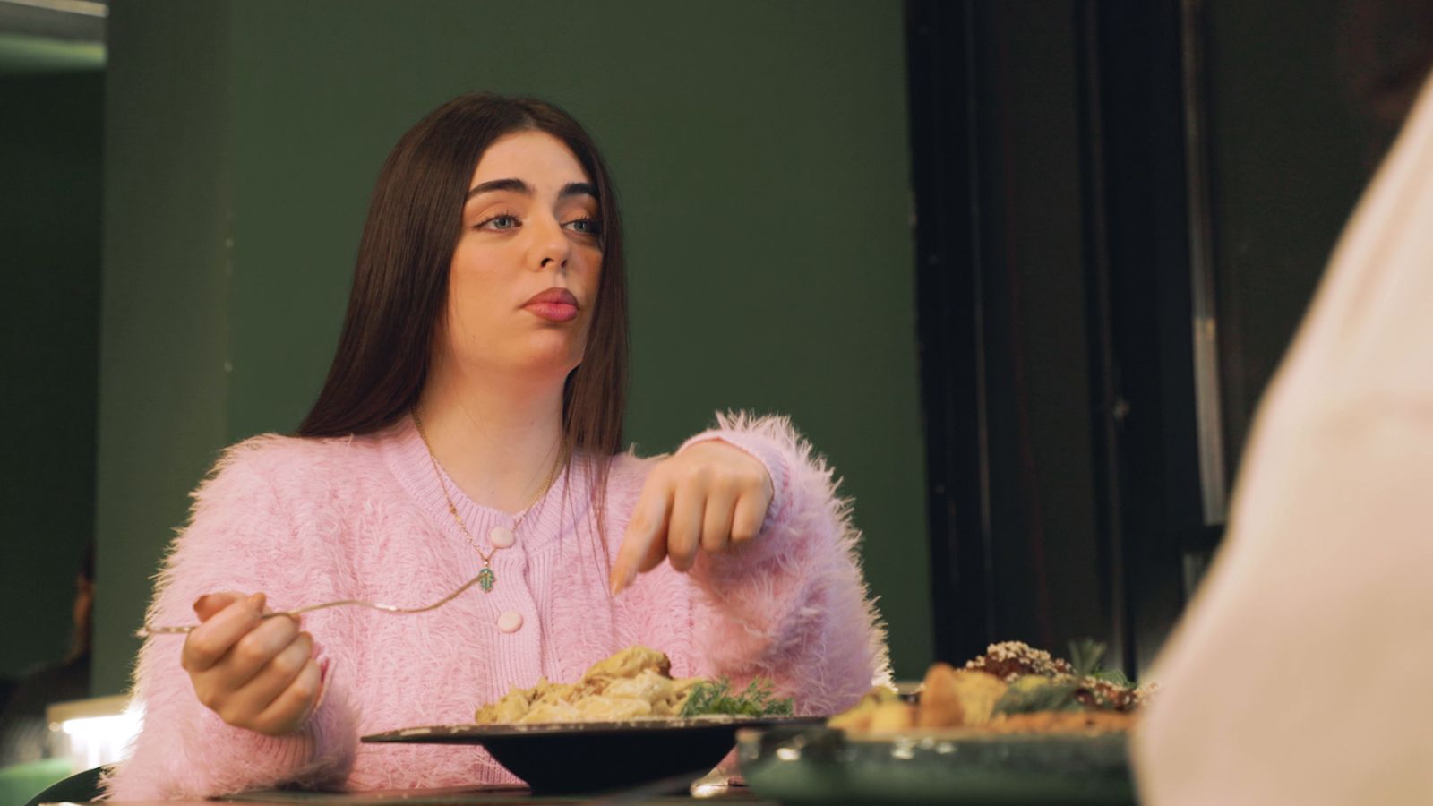 A woman in a pink sweater eating at a restaurant table