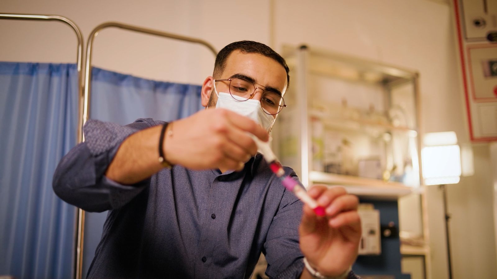 A lab technician in a mask preparing a blood sample tube