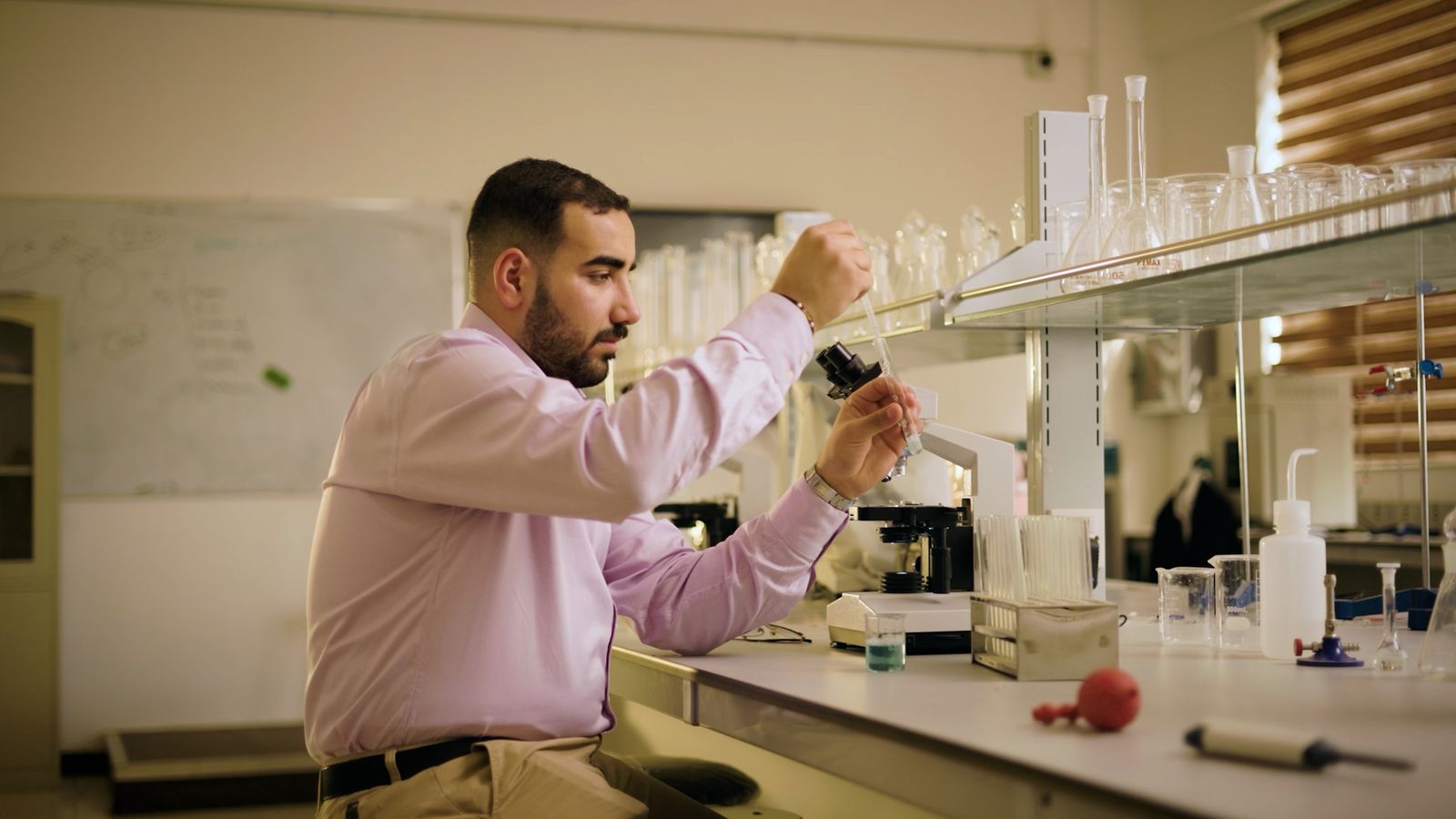 A scientist using a pipette beside a microscope in a laboratory
