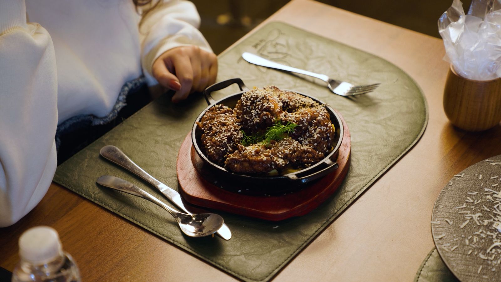 A sizzling skillet of sesame chicken on a green leather placemat