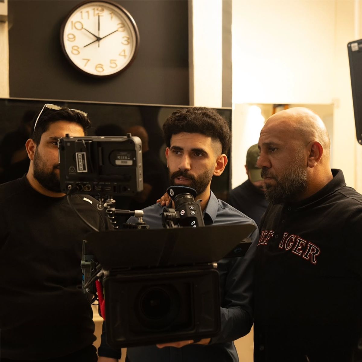 Three crew members around a camera in front of a wall clock