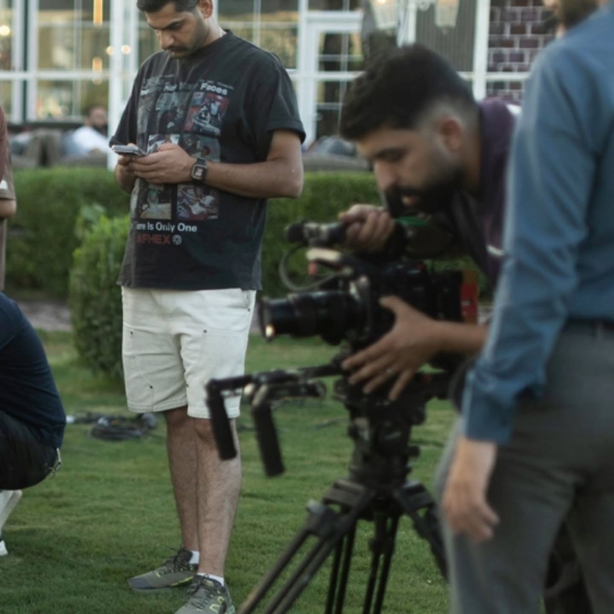 A camera operator at work while a crew member checks his phone