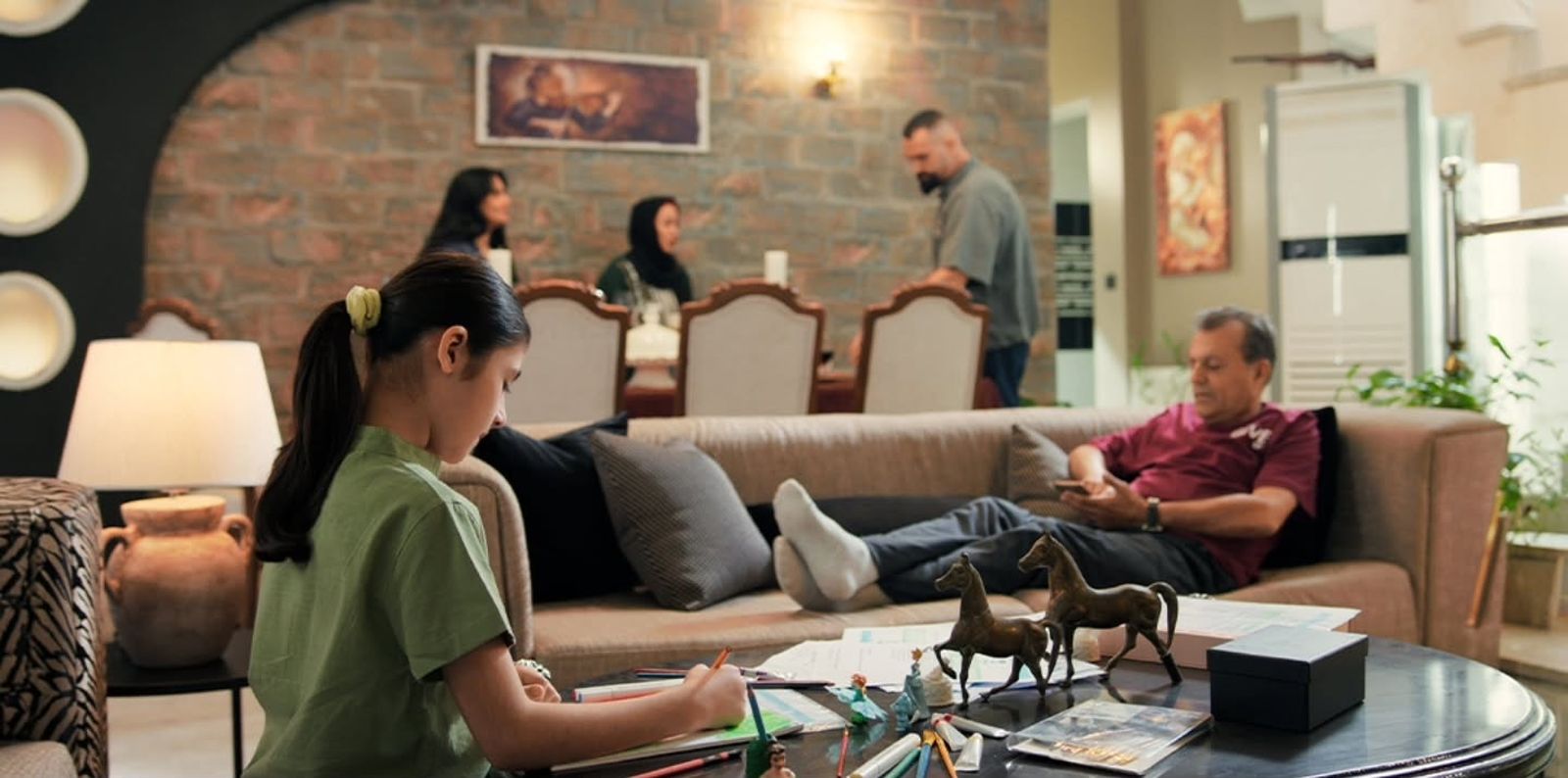 A girl drawing at a coffee table while her family relaxes at home