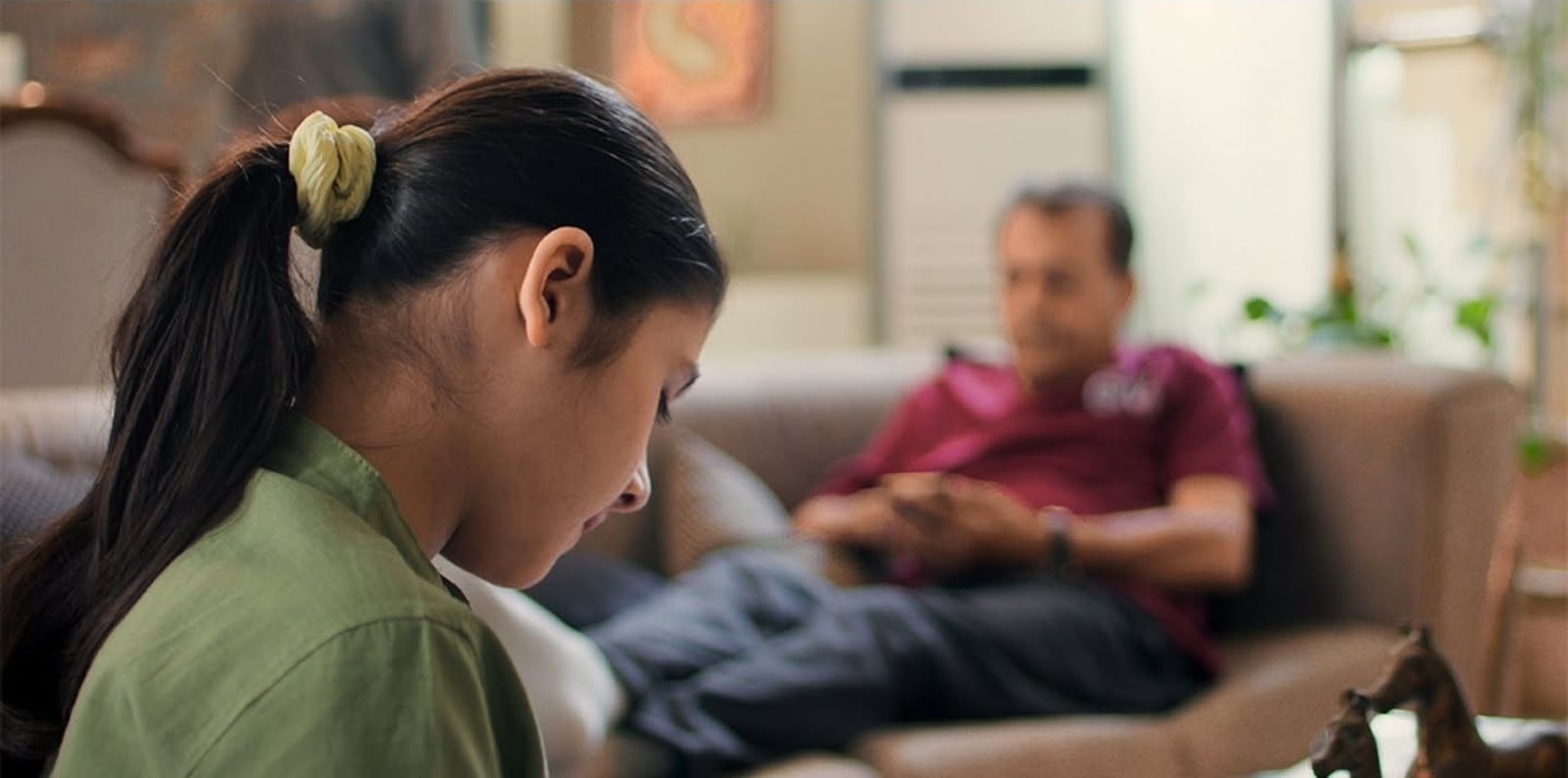 Close-up of a girl drawing with her father blurred behind her