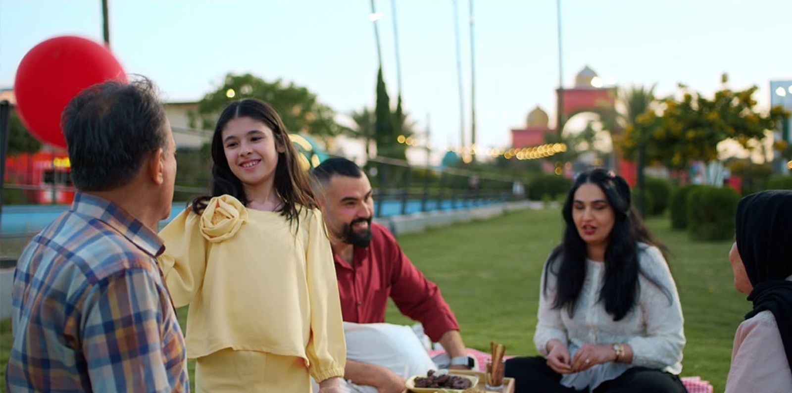 A girl in a yellow dress smiling beside her family at a picnic